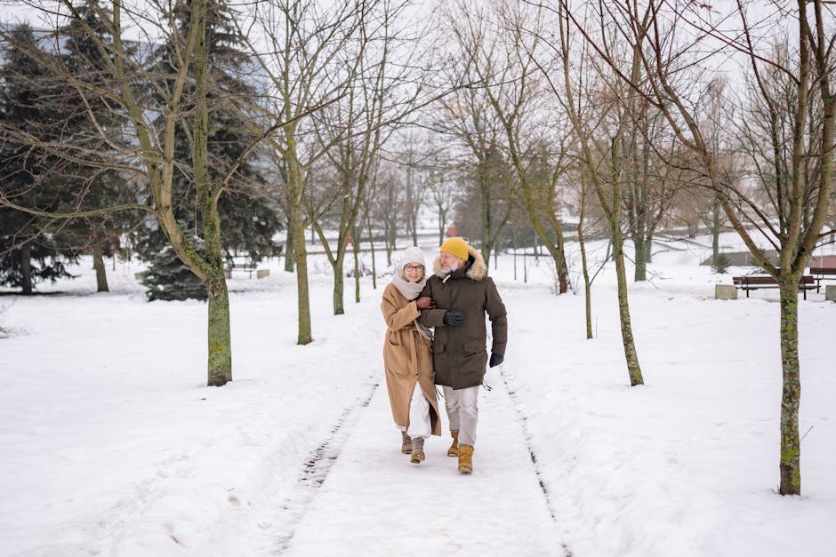 Happy senior couple walking arm-in-arm through a snowy park in winter.