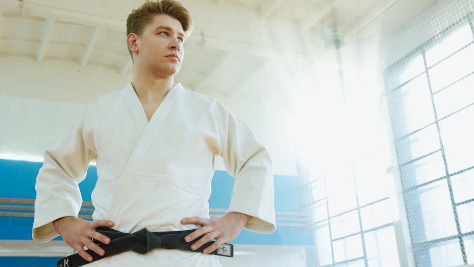 Young male martial artist in a white uniform, standing confidently indoors.