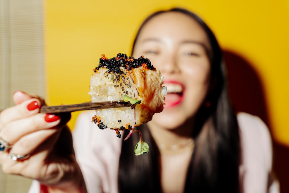 Close-up of sushi being eaten with chopsticks by a woman with a bright yellow background.
