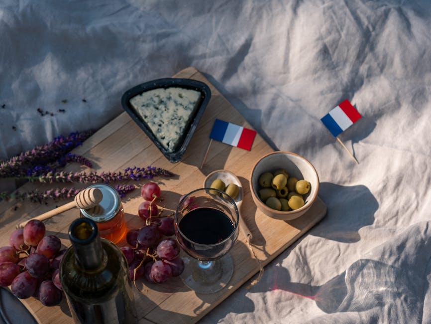 Top view of a French picnic setting with wine, blue cheese, grapes, and olives on a wooden board.