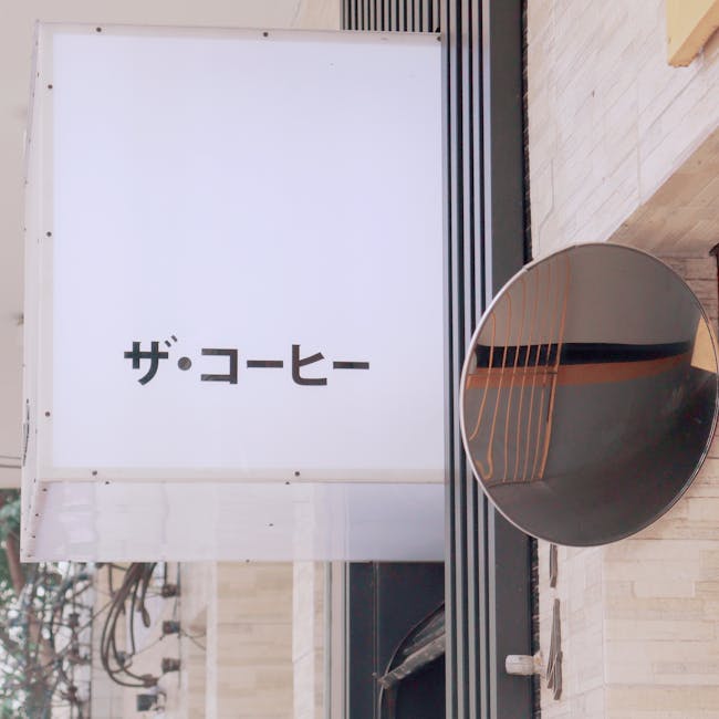 A modern Japanese coffee shop sign and reflective mirror on an urban street.