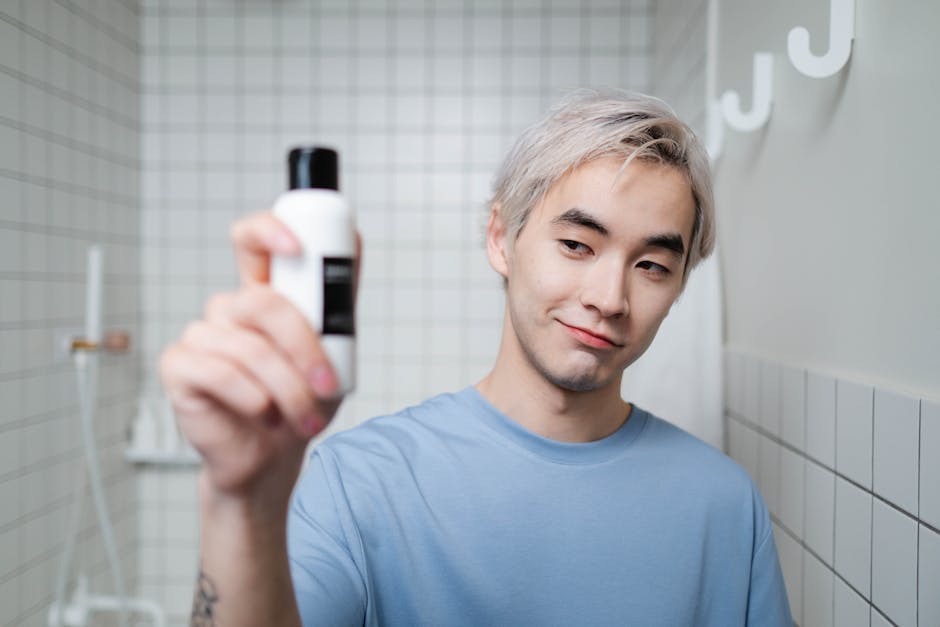 Portrait of a young man showcasing a skincare product in a modern bathroom setting.
