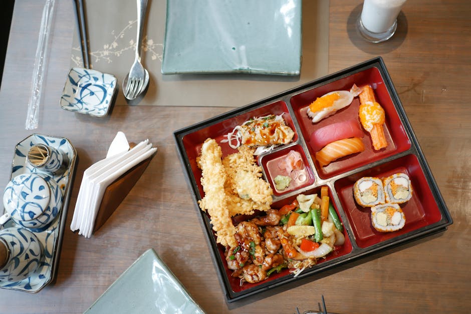 Japanese bento box meal with sushi, tempura, and vegetables arranged for a top view shot.