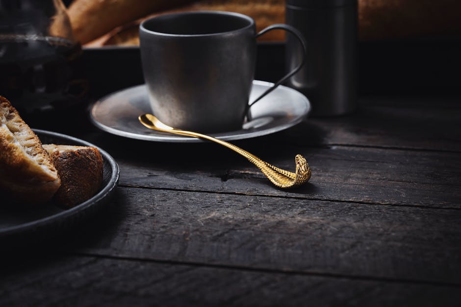 Stylish coffee setting featuring a gold snake-shaped spoon and rustic bread on a dark wooden table.