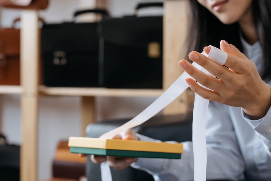Close-up of a woman holding a gift box with ribbon in an office setting, with briefcases in the background.