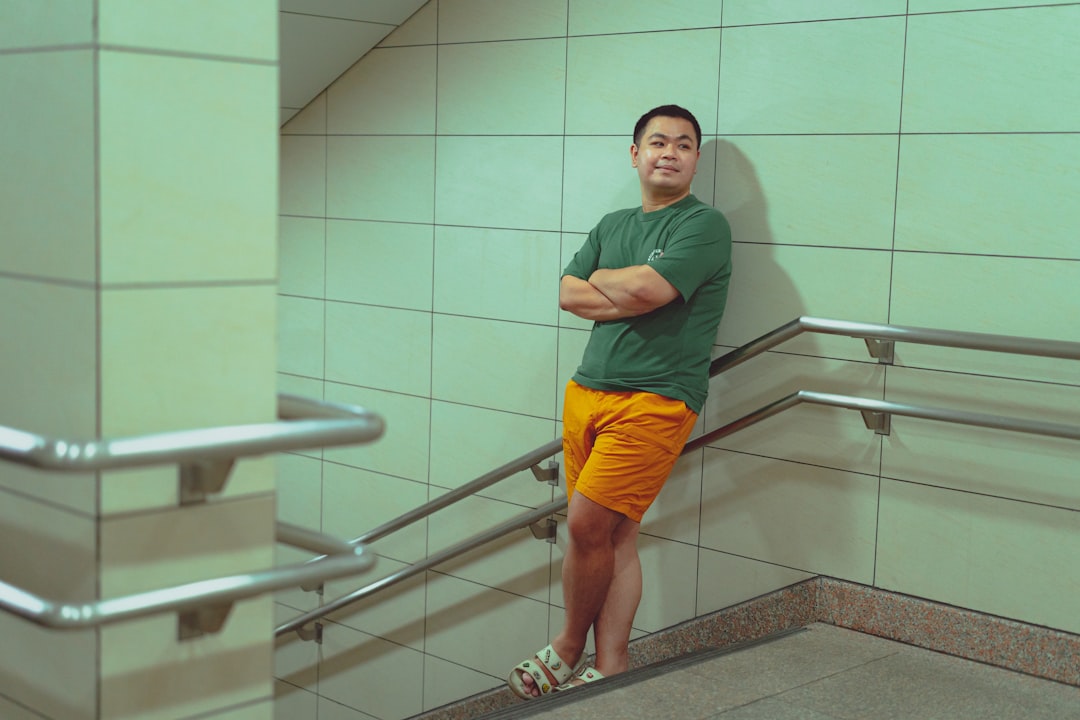 A man in green shirt and orange shorts leaning against a wall