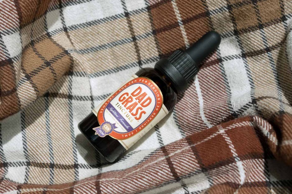 Close-up of Dad Grass CBD tincture bottle on plaid fabric, showcasing product branding.