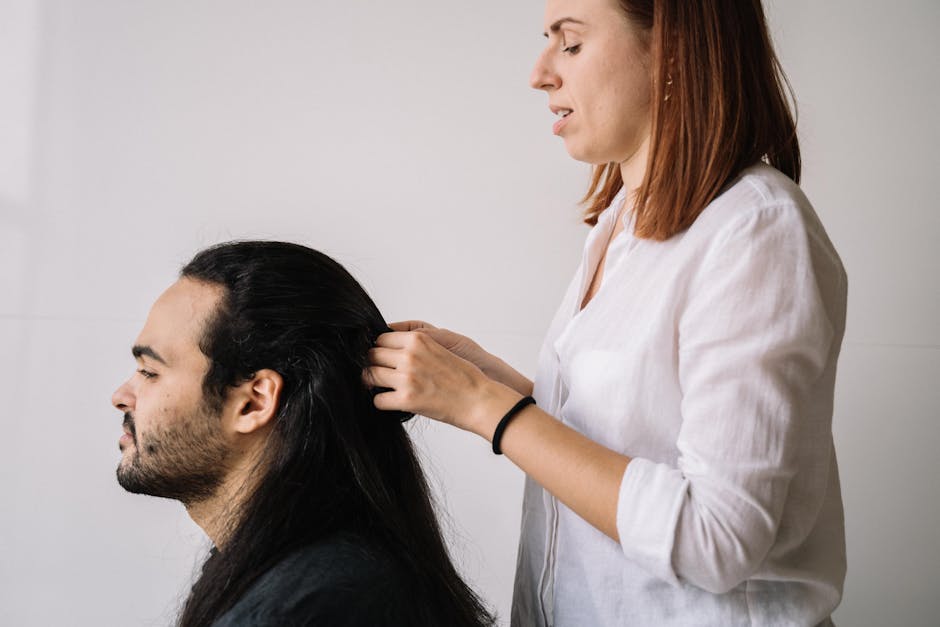 Professional hairdresser braiding a man's long hair, focusing on style and modern grooming.