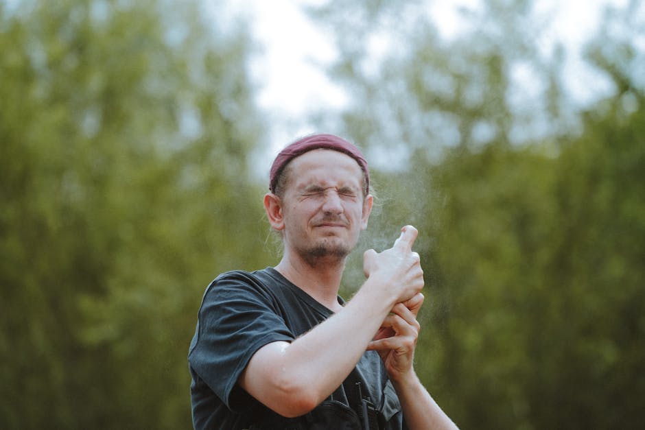 A man squints his eyes while spraying outdoors, creating a misty effect in the natural setting.