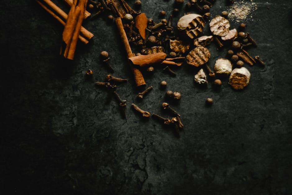 A collection of aromatic spices including cinnamon and cloves on a textured dark background.