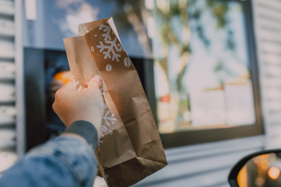Hand reaching out with brown paper bag at drive-thru window, showcasing casual takeout.