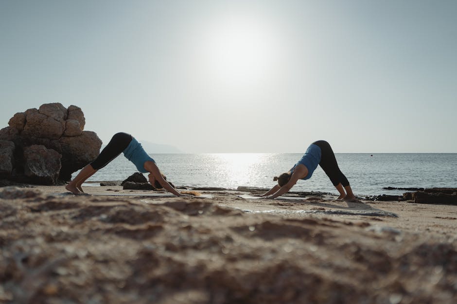 Two women practicing yoga at dawn on a serene beach with clear waters.