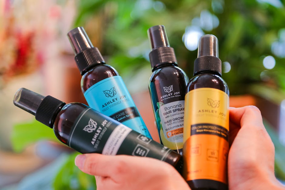 Close-up of hands holding various Ashley Joy hair care bottles with a blurred natural background.