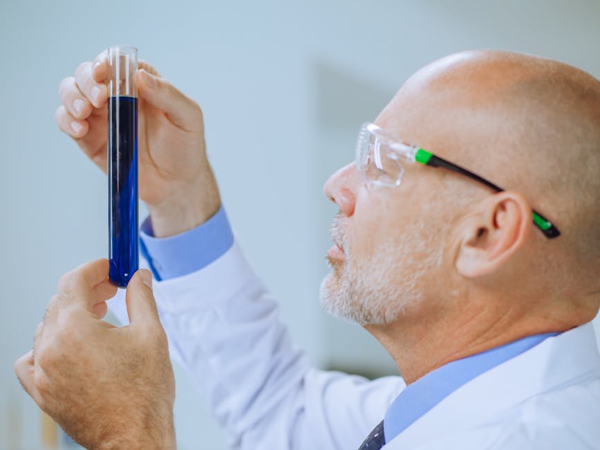 Scientist in lab coat examines a blue liquid in a test tube, showcasing focus and concentration.