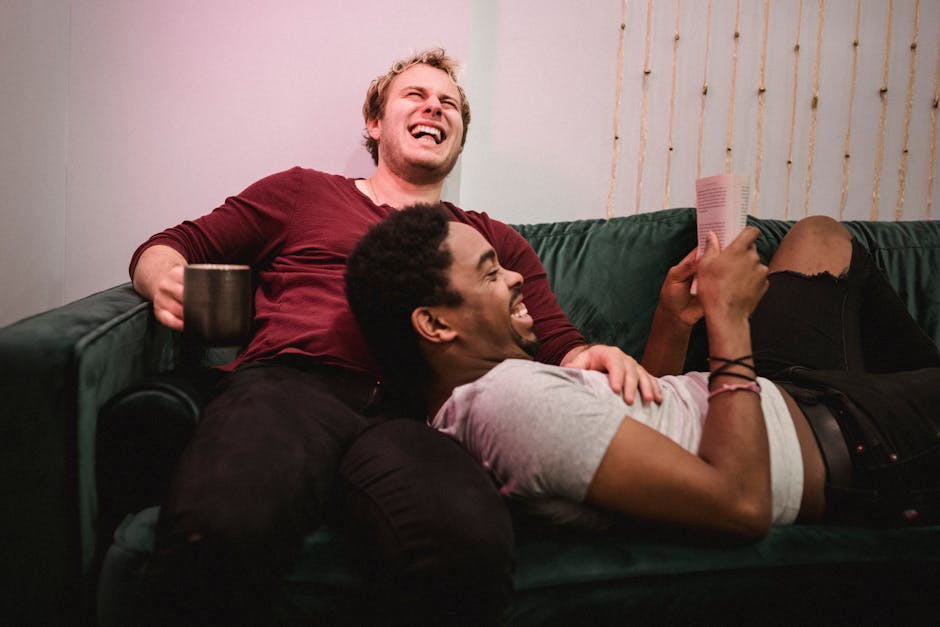 A happy interracial gay couple laughing and relaxing on a sofa indoors.